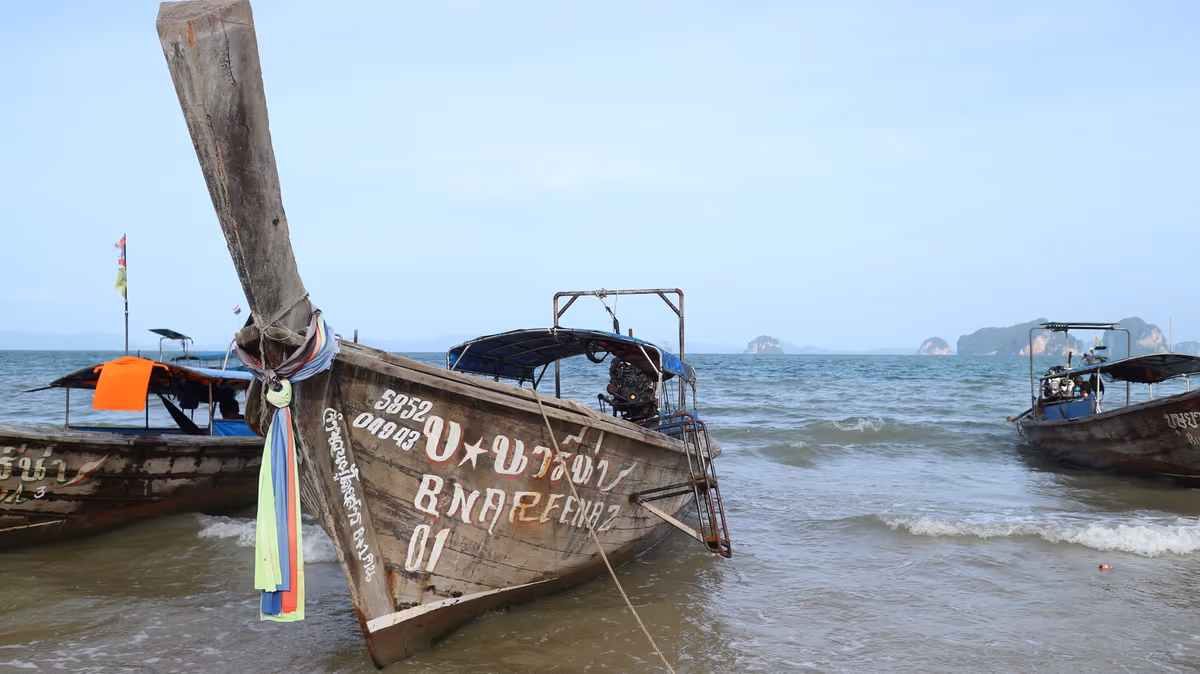 Bateau longtail thaïlandais traditionnel échoué sur la plage avec des îlots calcaires au loin
