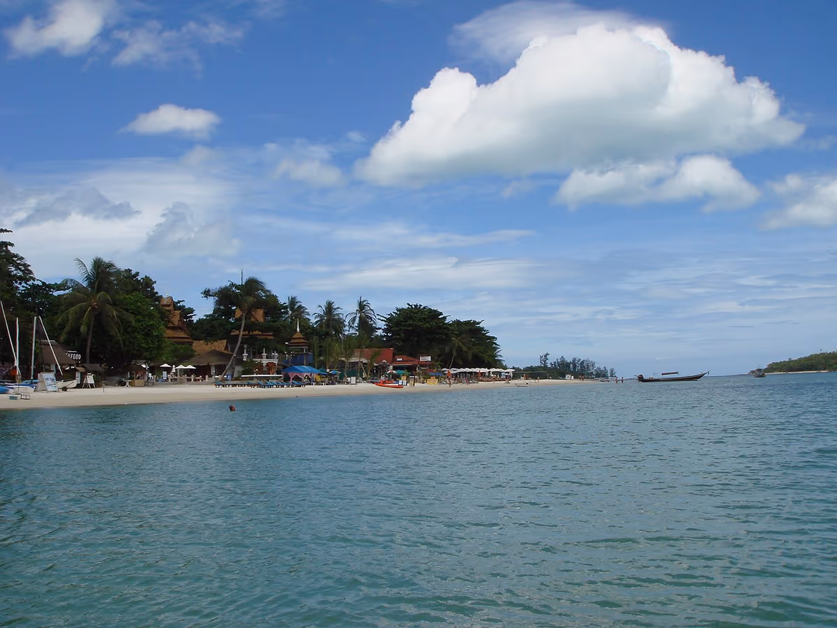 Plage de sable de Chaweng à Koh Samui avec bars en bord de mer, palmiers et bateau longtail