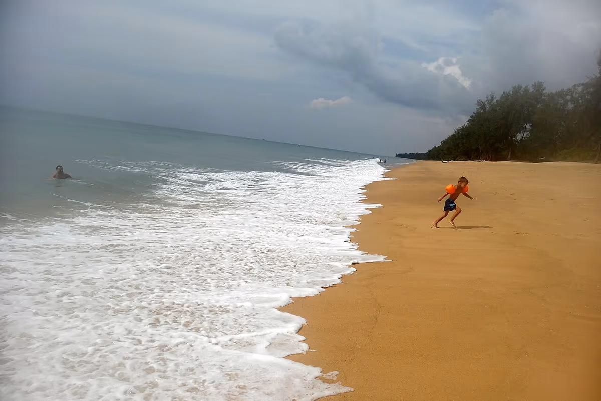 Mai Khao Beach in Phuket with waves and a child running on the sand